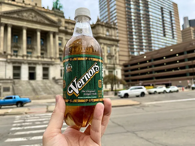 Author holding a bottle of Vernor's against a backdrop of downtown Detroit in Detroit Michigan