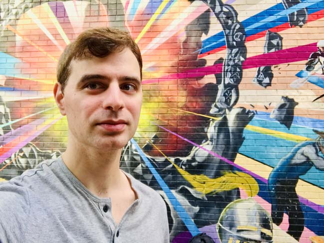 US travel blogger Michael DeFranceschi behind a colorful mural in uptown Charlotte, North Carolina.